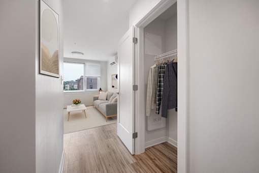 A room with a white wall and a wooden floor with a white sofa and a table with a vase of flowers on it.