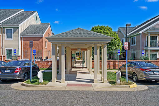 A small building with a porch is in front of a parking lot.