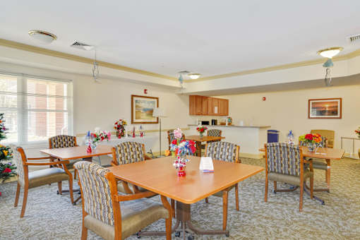 A dining room with a Christmas tree and chairs around a table.