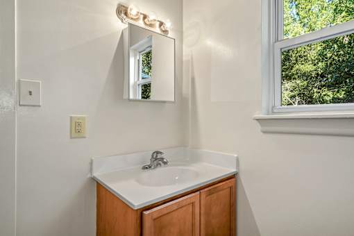A bathroom with a white sink and a mirror with lights on it.