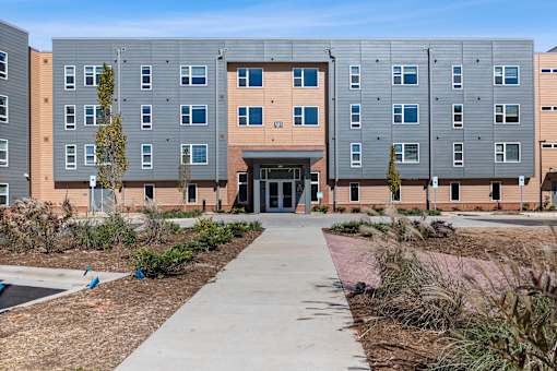 A modern building with a grey and orange facade and a walkway leading to the entrance.