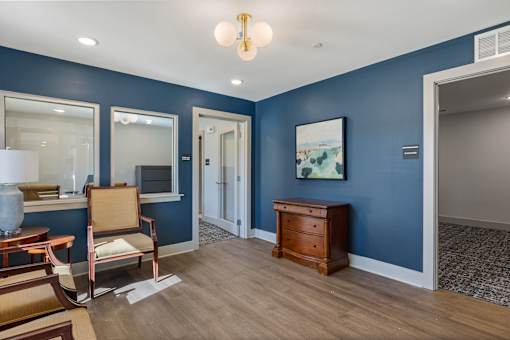 A room with blue walls and wooden floors has a chair, a table, and a painting on the wall.