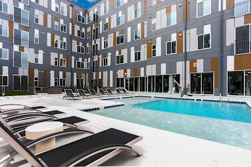 A large indoor swimming pool with lounge chairs and a building with balconies in the background.