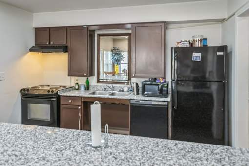 A kitchen with a black fridge, white countertop, and brown cabinets.
