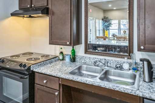 A kitchen with a stove, sink, and a mirror reflecting a dining area.