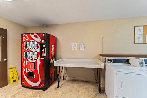A red soda machine sits next to a white washing machine in a room.