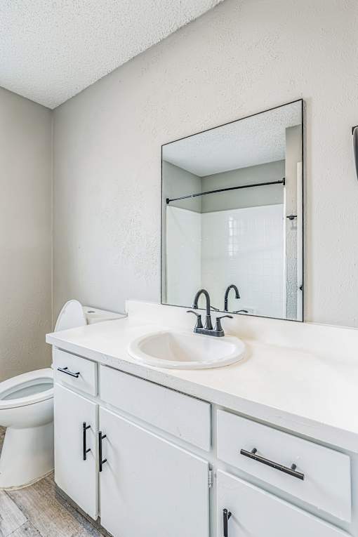 A white bathroom with a sink, mirror, and toilet.