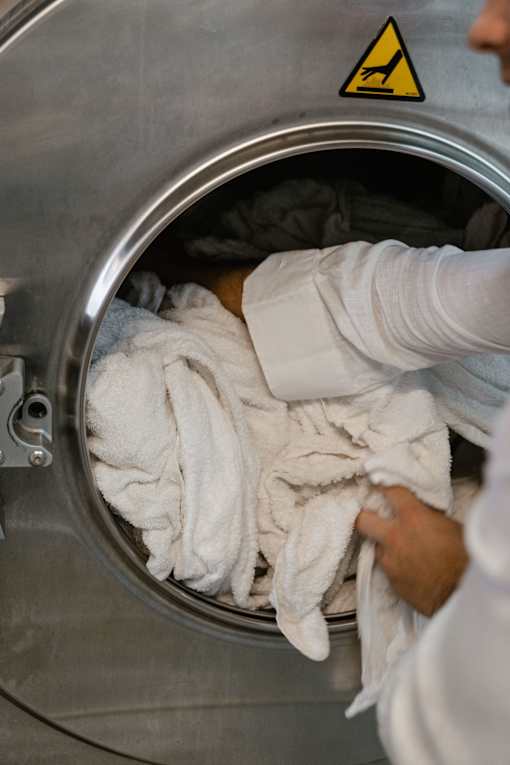 A person is taking out a white towel from a stainless steel washing machine.