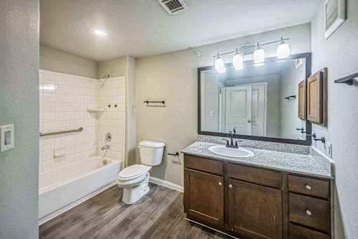 A bathroom with a white toilet, a wooden cabinet, and a large mirror.
