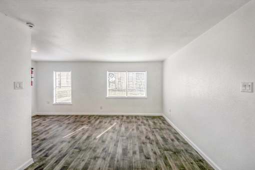 A room with wooden flooring and two windows.