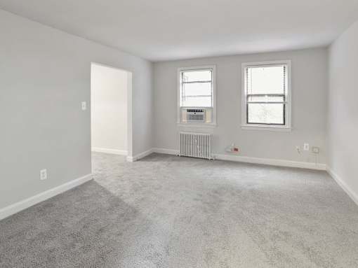 A sparsely furnished room with a carpeted floor and two windows.