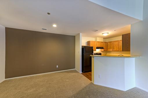 a empty living room with a kitchen with a black refrigerator