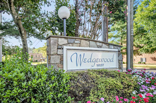 A sign that says "Wedgewood West" is surrounded by greenery and flowers.