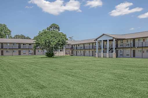A large grassy field in front of a building with a tree in the middle.