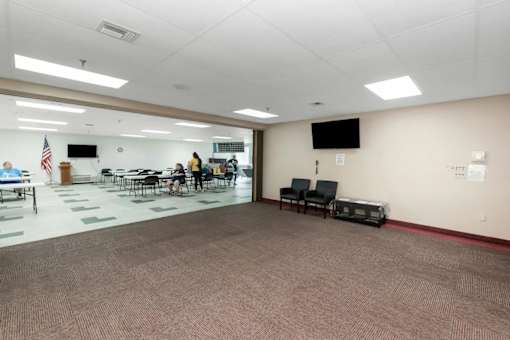 A room with a carpeted floor and a few chairs and tables.