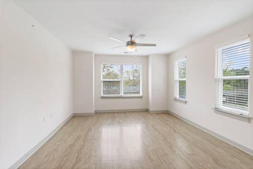 A room with a ceiling fan and two windows.