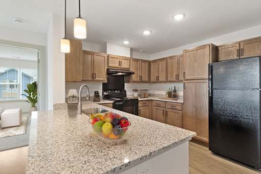 A kitchen with a black refrigerator and a bowl of fruit on the counter.