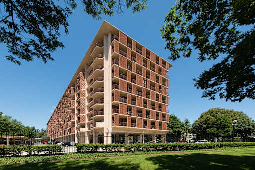 A tall red brick building with a triangular top is surrounded by trees and greenery.