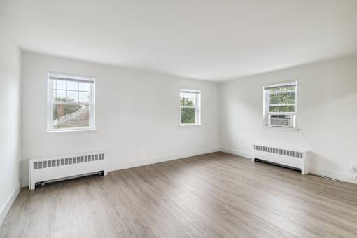 an empty room with white walls and wood floors and two windows
