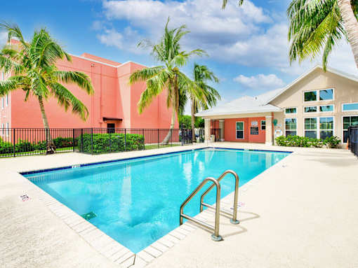 A swimming pool surrounded by palm trees and a red building.
