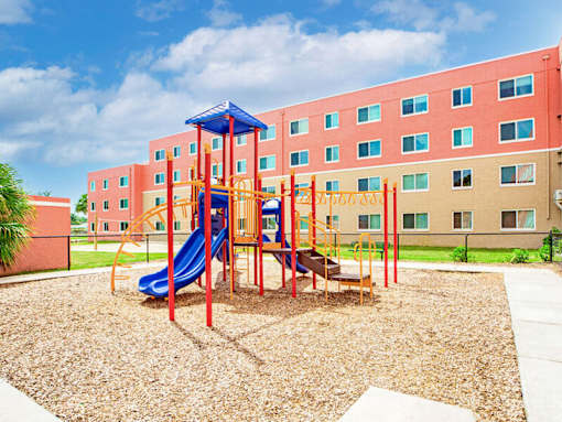 A playground with a blue slide and a red and yellow structure in front of a red building.