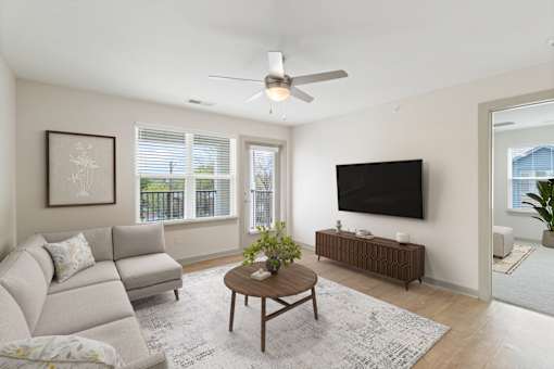 A living room with a grey couch, a coffee table, a flat screen TV and a ceiling fan.
