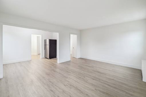 an empty living room with white walls and a refrigerator