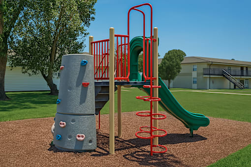 A playground with a green slide and a grey structure with red rings.