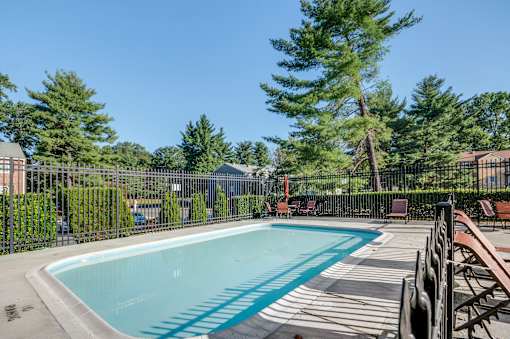 A pool surrounded by trees and chairs.