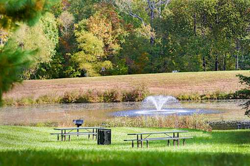 A fountain in the middle of a grassy field with picnic tables nearby.