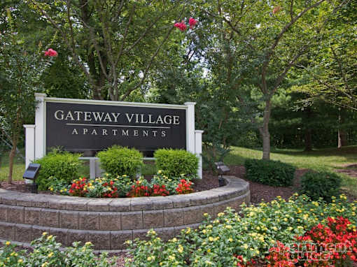 A sign for Gateway Village Apartments is surrounded by flowers and greenery.