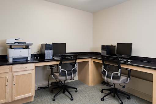 A room with two desks and chairs, one of which has a monitor on it.