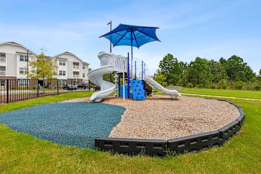A playground with a blue umbrella and a slide.