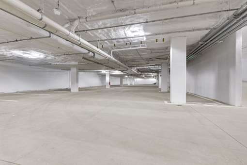 A long hallway with white pillars and pipes on the ceiling.