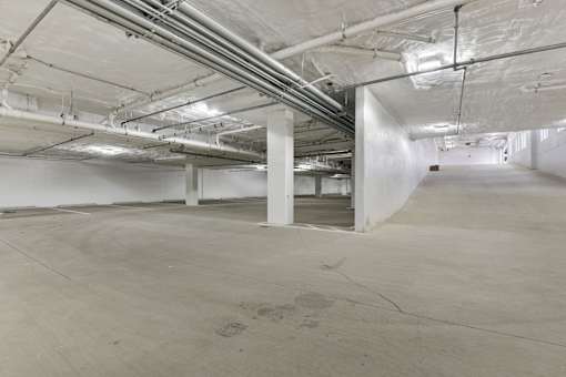 A large, empty, industrial-style room with concrete floors and exposed pipes and ducts.