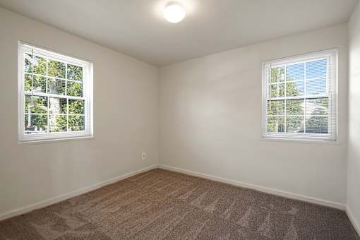 A room with two windows and carpeted flooring.