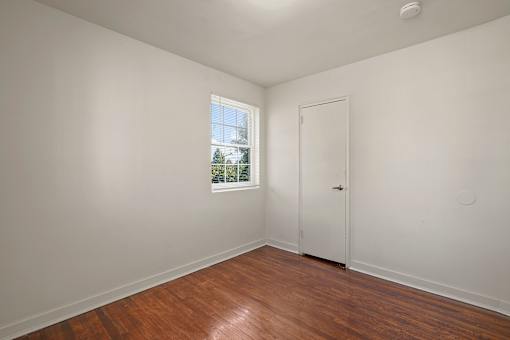 A room with a white door and a window with a view of trees and a house outside.