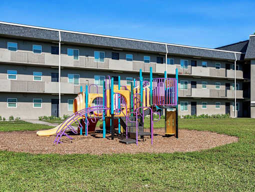 A playground with a slide, swings, and a monkey bars set in front of a building.