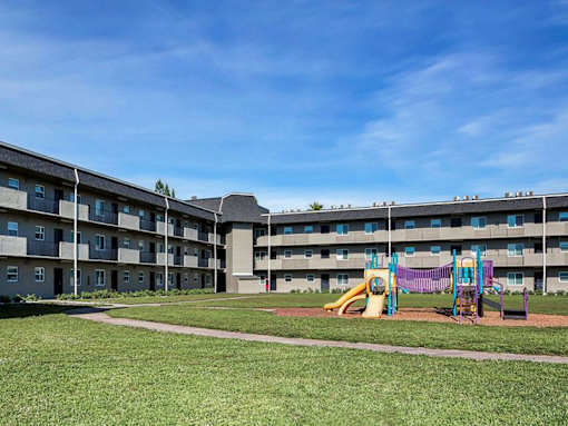 A playground with a slide and swings is in front of a large apartment building.