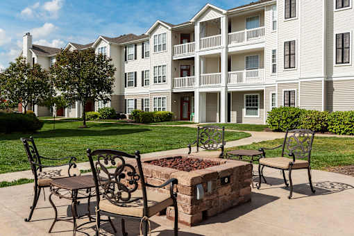 A patio with a fire pit and chairs in front of a building.