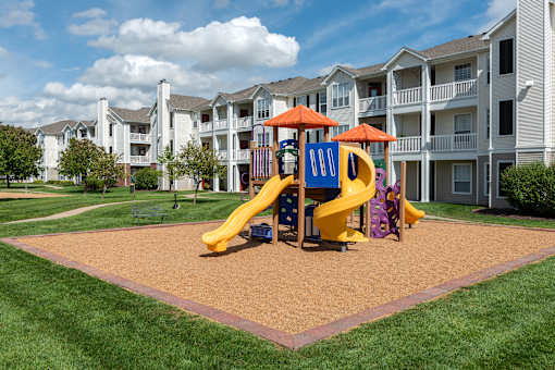 A playground with a yellow slide and a purple slide in front of apartment buildings.
