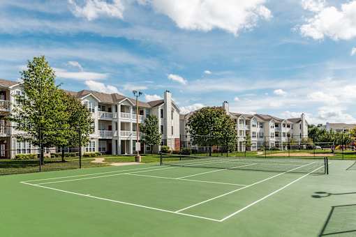 A tennis court is surrounded by apartment buildings.