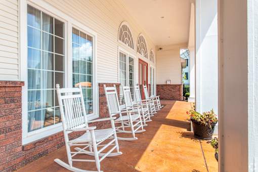 A porch with white rocking chairs and a brick wall.