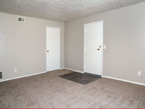 an empty living room with carpet and two doors