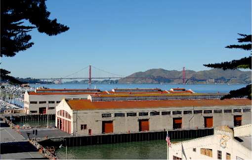 A large building with a red roof is in the foreground with a bridge in the background.