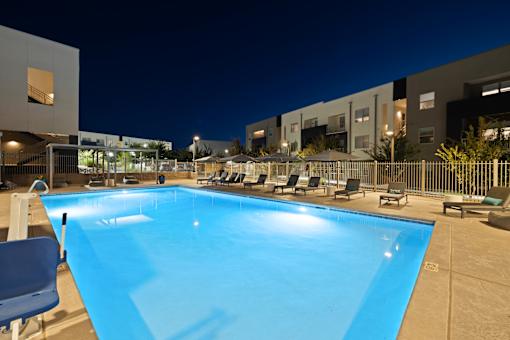 A swimming pool surrounded by chairs and umbrellas at night.