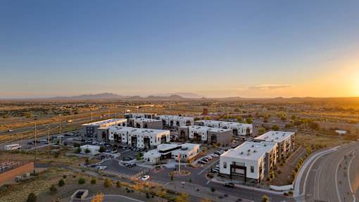 A sunset view of a modern building complex surrounded by a parking lot.