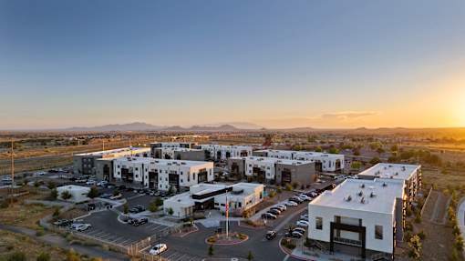 A sunset view of a modern building complex with a parking lot in the foreground.