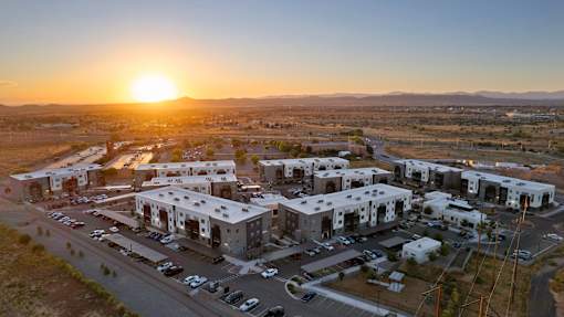 A sunset view of a parking lot with several cars and a building complex.