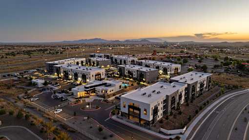 A modern building complex is lit up at dusk with a mountain range in the background.